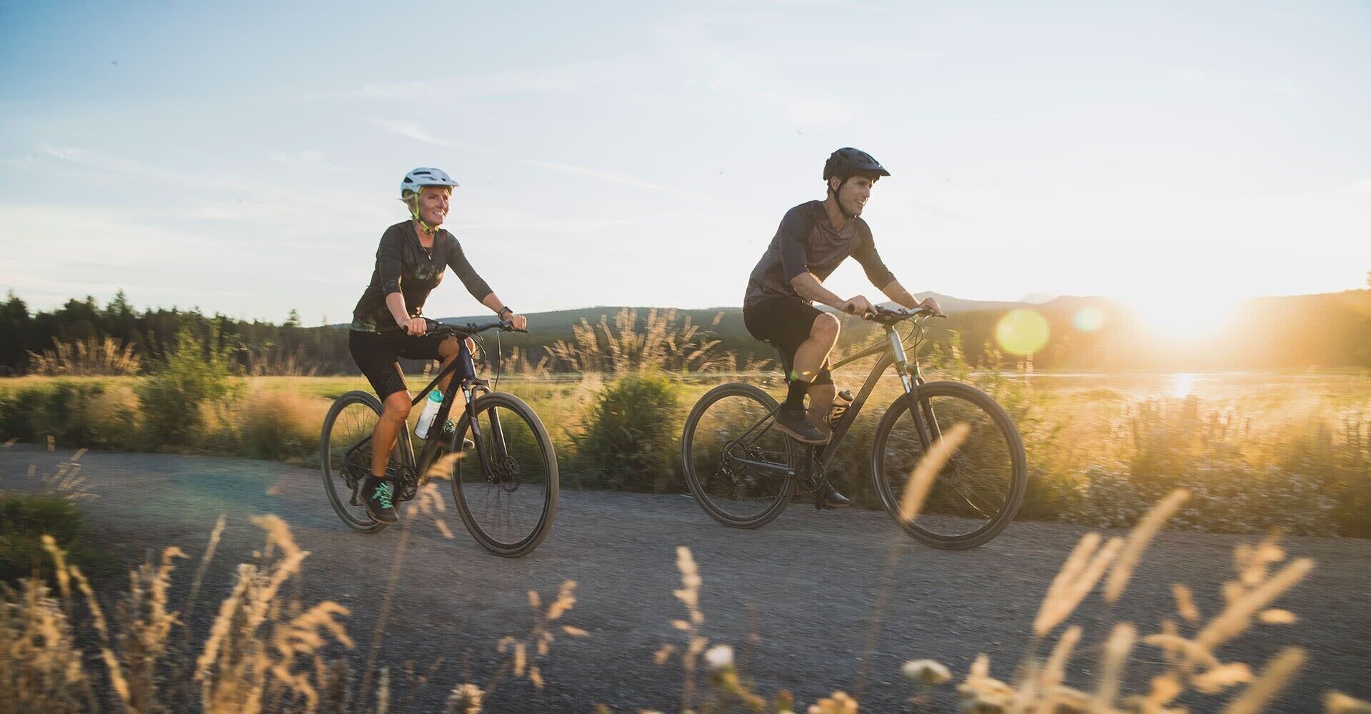 Two cyclists on a paved path with a natural landscape in the background.