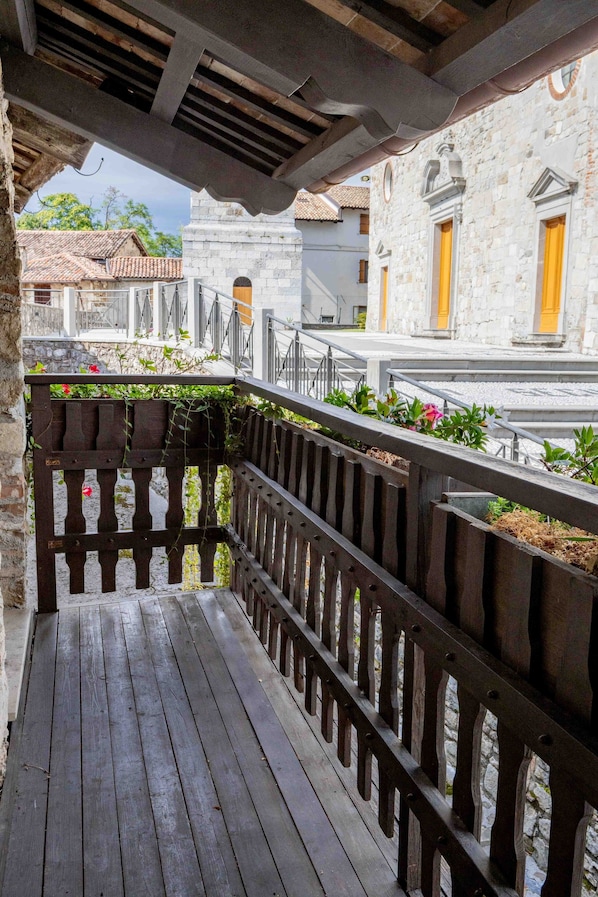 A wooden balcony with a metal railing, overlooking a street with traditional buildings and a clear sky.
