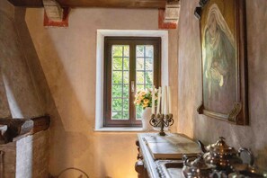 Una habitació amb finestra, un quadre, una taula amb un ram de flors i una cuina.