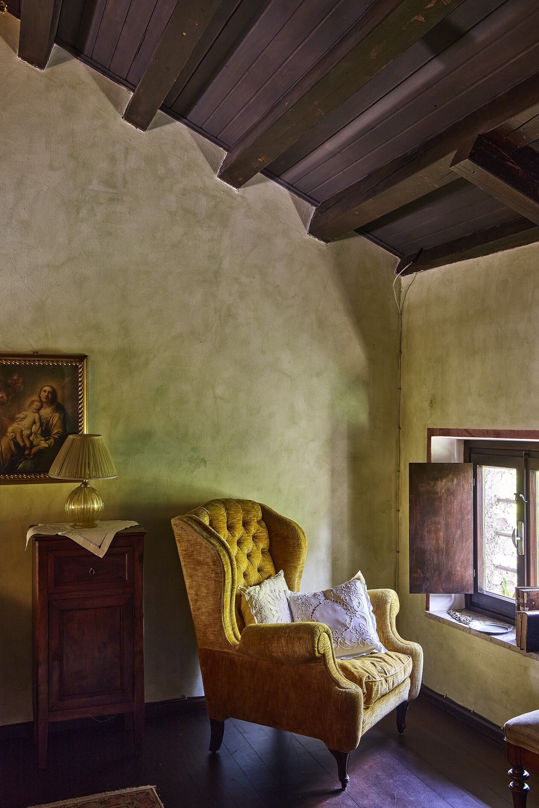 A room with a vintage armchair, a lamp, and a painting on the wall.