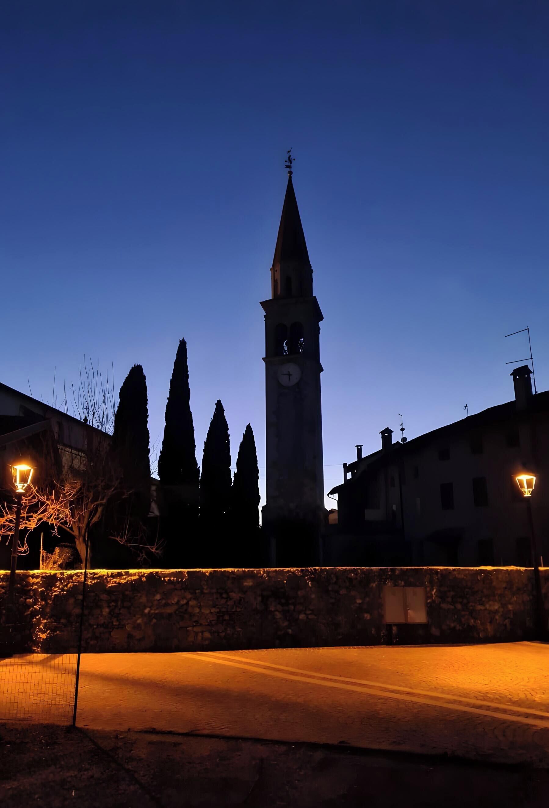 A clock tower with a weather vane, surrounded by trees and buildings.