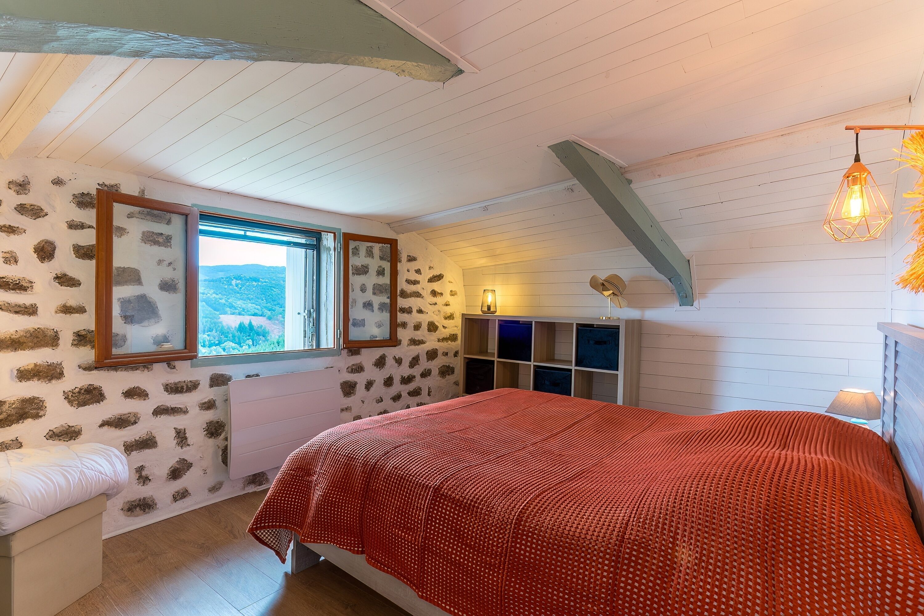 A bedroom with a bed, a window with a view, a built-in wardrobe, and a sloped ceiling.