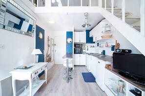 A modern kitchen with white cabinets, a black TV, and a blue accent wall. - L'Écrin Bleu - À 300 m de la plage (Argeles-sur-Mer)
