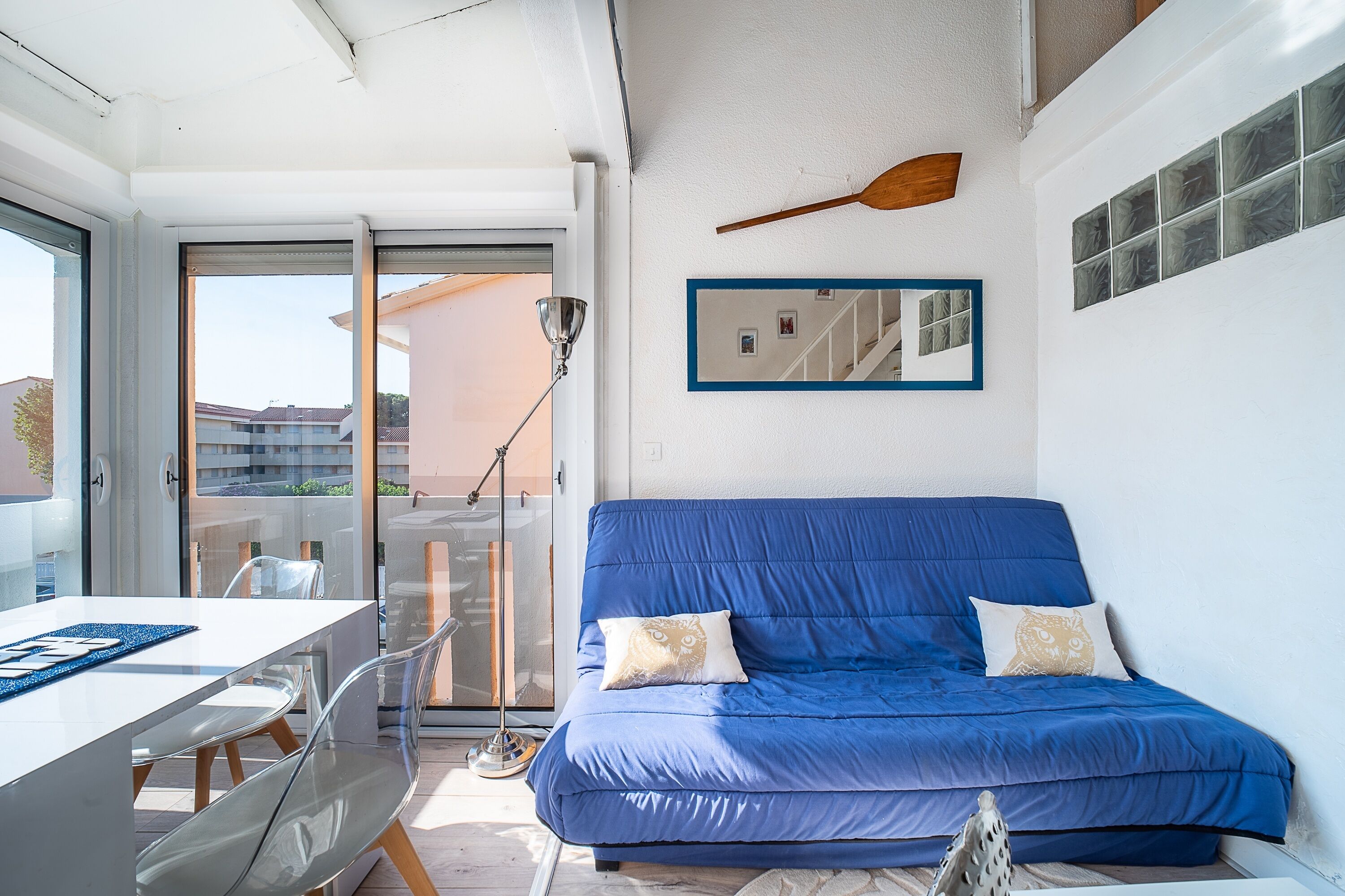 Une pièce moderne avec un canapé bleu, une table à manger et une vue sur l’extérieur, visible à travers une porte vitrée.
