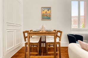 A dining area with a wooden table set for six, a white wall with a 'TOULOUSE' poster, and a window with a view of buildings. - Confidence - À 400 m du métro Jeanne d'Arc (Toulouse)