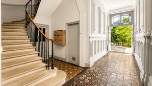 A grand staircase with a wooden handrail, a patterned floor, and a view of a lush garden through an open door. - Confidence - À 400 m du métro Jeanne d'Arc (Toulouse)