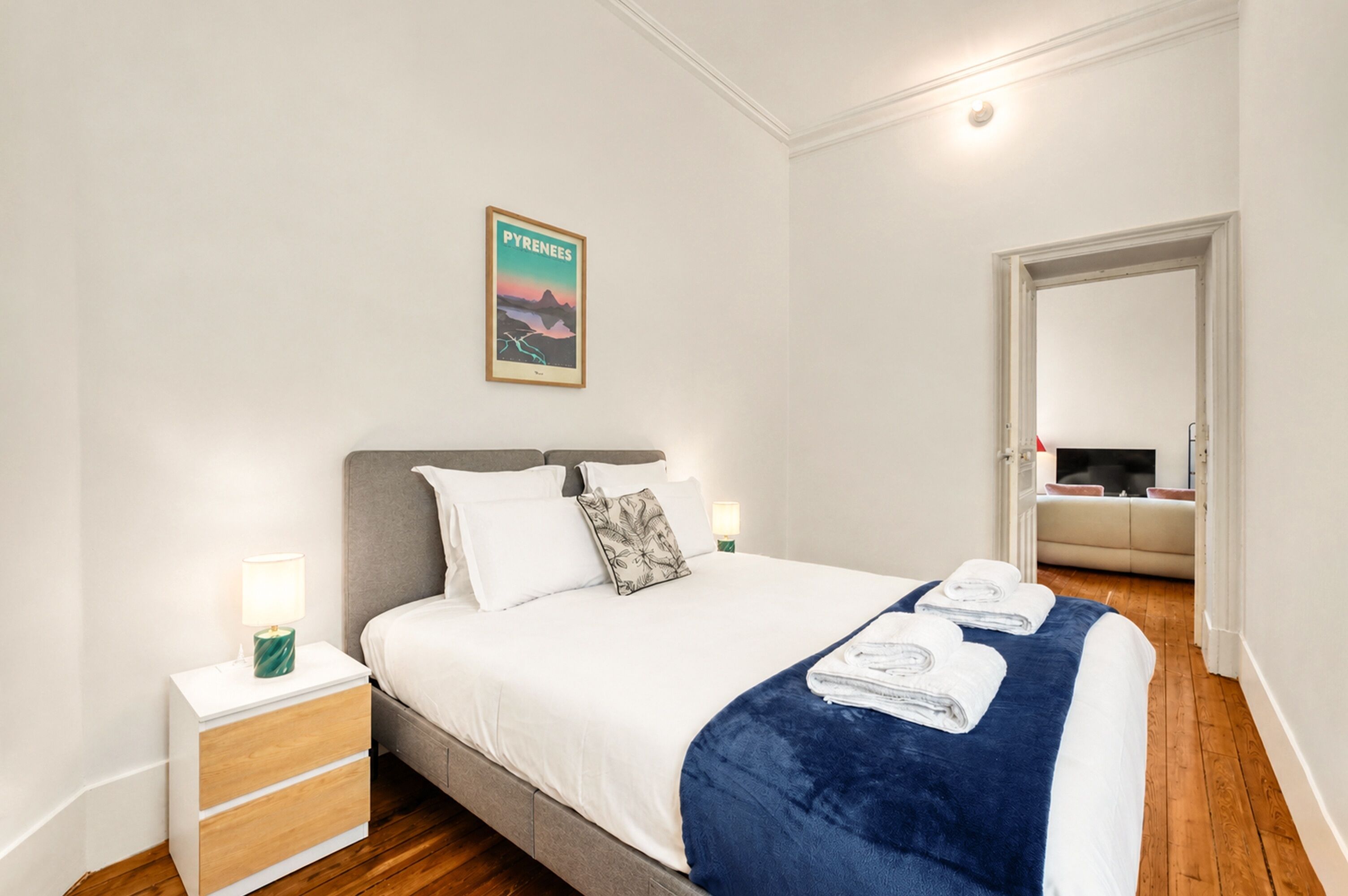 A bedroom with a bed, nightstands, a framed picture, and a door leading to another room.