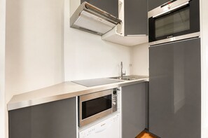 Ett kompakt kök med inbyggd ugn, mikrovågsugn och diskmaskin, med en modern design och vitvaror i rostfritt stål.