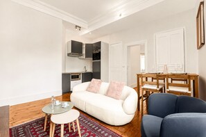 Un salon moderne comprenant un canapé, un fauteuil bleu, une petite table ronde et un coin repas avec une table et des chaises en bois.
