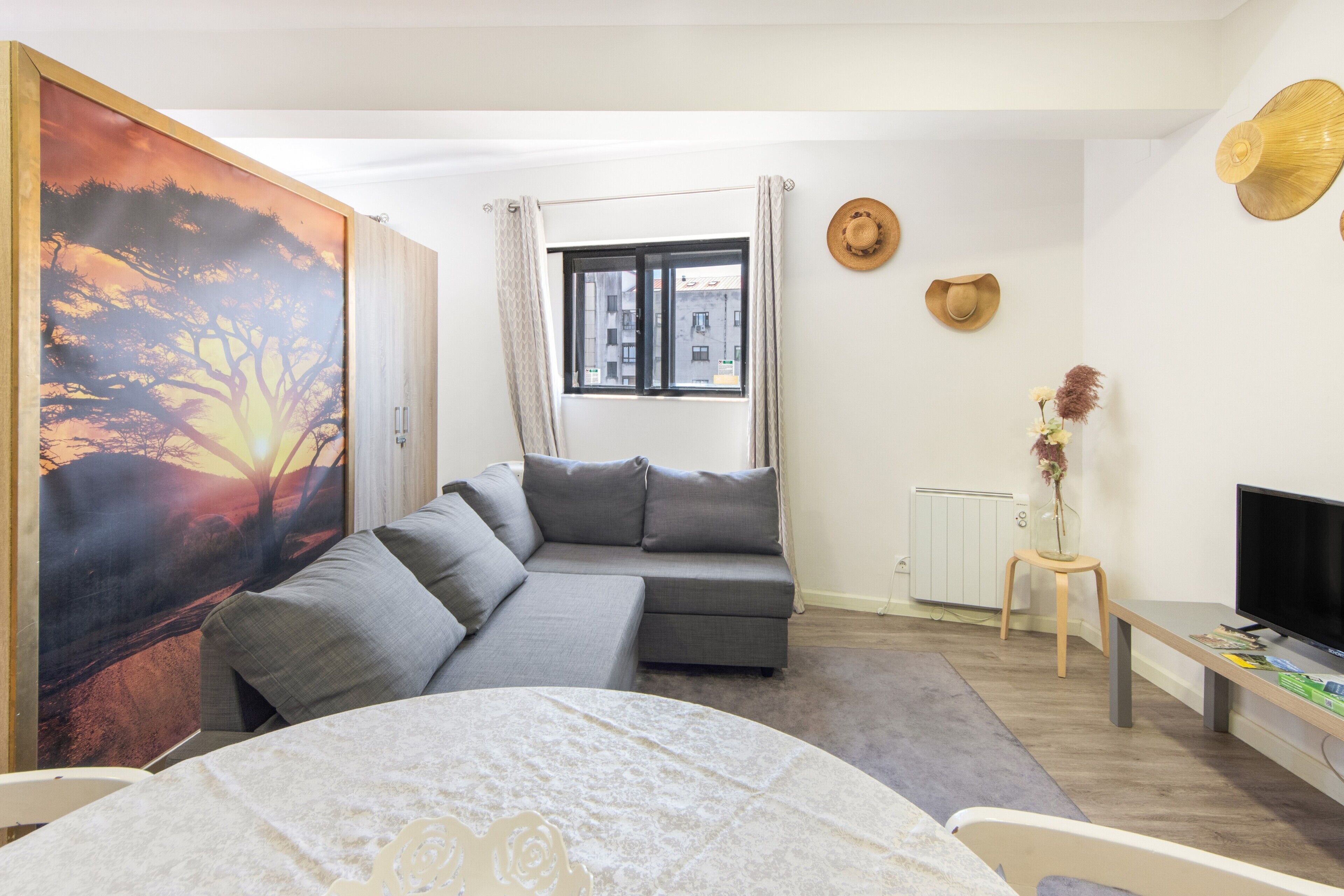 Un salon moderne avec un canapé gris, un téléviseur et un tableau représentant un coucher de soleil.