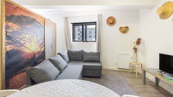 Un salon moderne avec un canapé gris, un téléviseur et un tableau représentant un coucher de soleil.