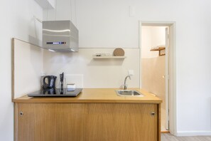 A modern kitchen with a stainless steel range hood, a wooden countertop, a sink, and a small shelf with kitchen items. - Apartment 'Praça AL T1' with Mountain View, Wi-Fi and Air Conditioning (São João da Madeira)
