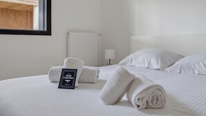 A neatly made bed with white linens and a rolled towel, a white pillow, and a sign on the bed. - Les Perles de l’Aiguillon - Appt face au bassin (La Teste-de-Buch)