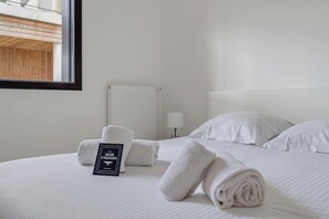 Ein ordentlich bezogenes Bett mit weißen Laken, ein aufgerolltes Handtuch und ein Schild am Bett.
