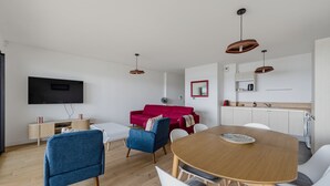 A modern living room with a dining table, a red sofa, and a TV mounted on the wall. - Les Perles de l’Aiguillon - Appt face au bassin (La Teste-de-Buch)