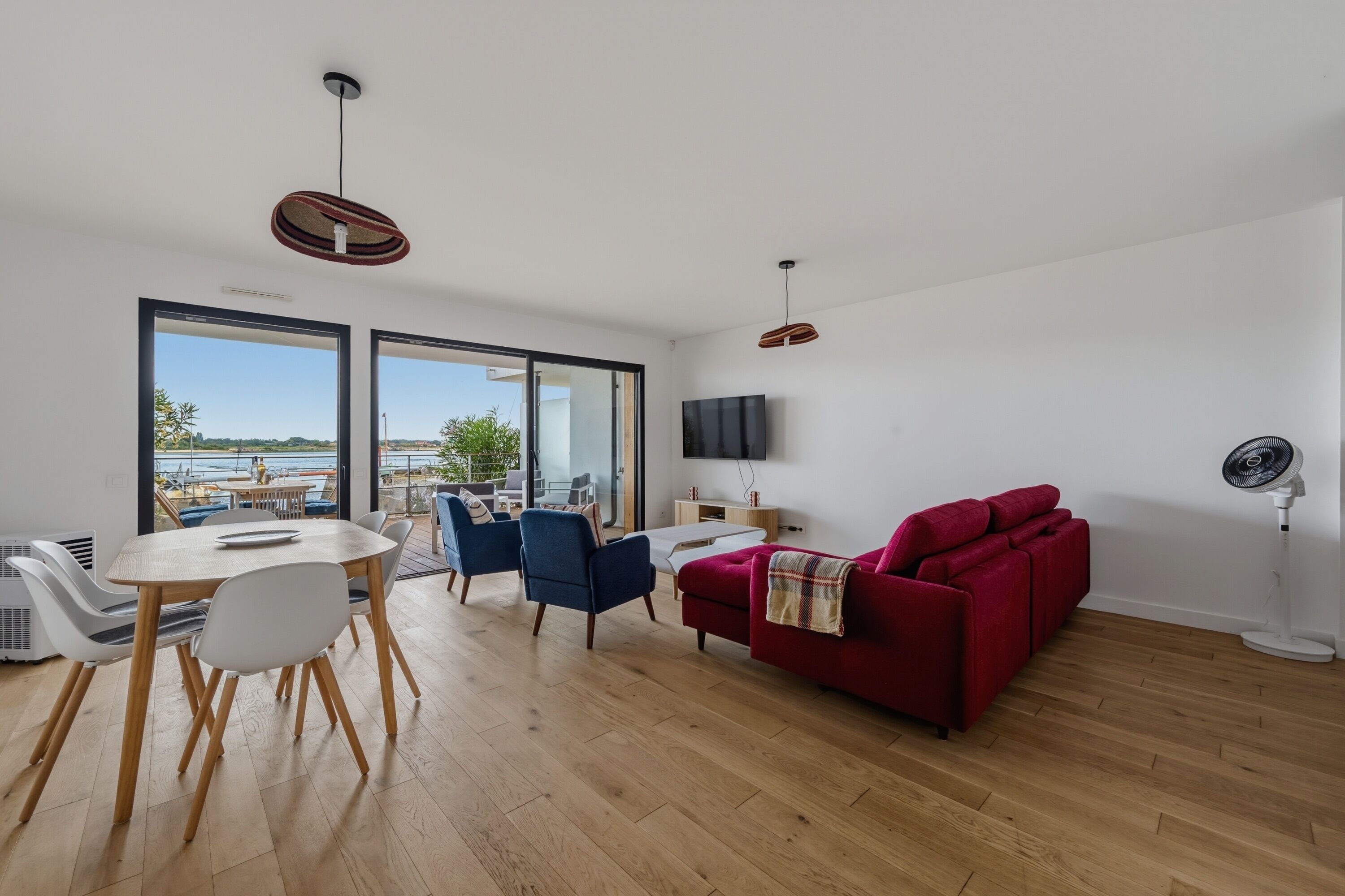 A modern living room with a dining area, a red sofa, a TV, and a large window with a view.