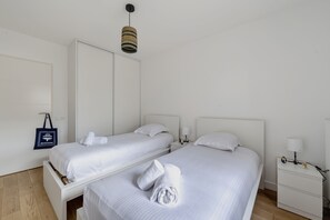 Ein Hotelzimmer mit zwei Betten, einem Nachttisch mit Lampe, einem an der Wand befestigten Handtuchhalter und einer Pendelleuchte.