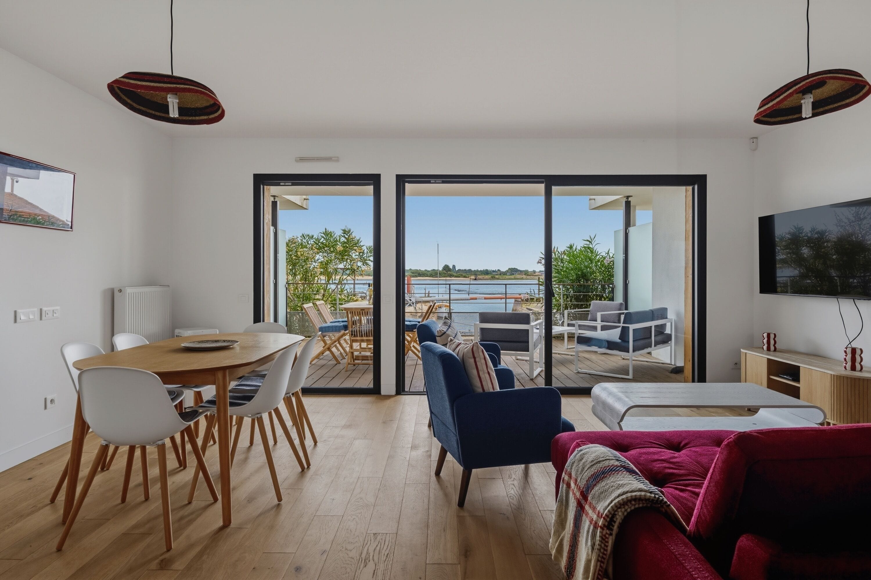 A modern living room with a dining area, a TV, and a view of a body of water.