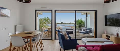 A modern living room with a dining area, a TV, and a view of a body of water.