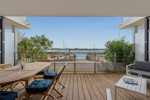 Eine Terrasse im Freien mit Holzboden, Sitzgelegenheiten und Blick auf das Meer.