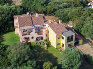 A two-story house with a tiled roof, multiple balconies, and a patio area with outdoor furniture. - Comfortable and Bright Apartment (Stintino)