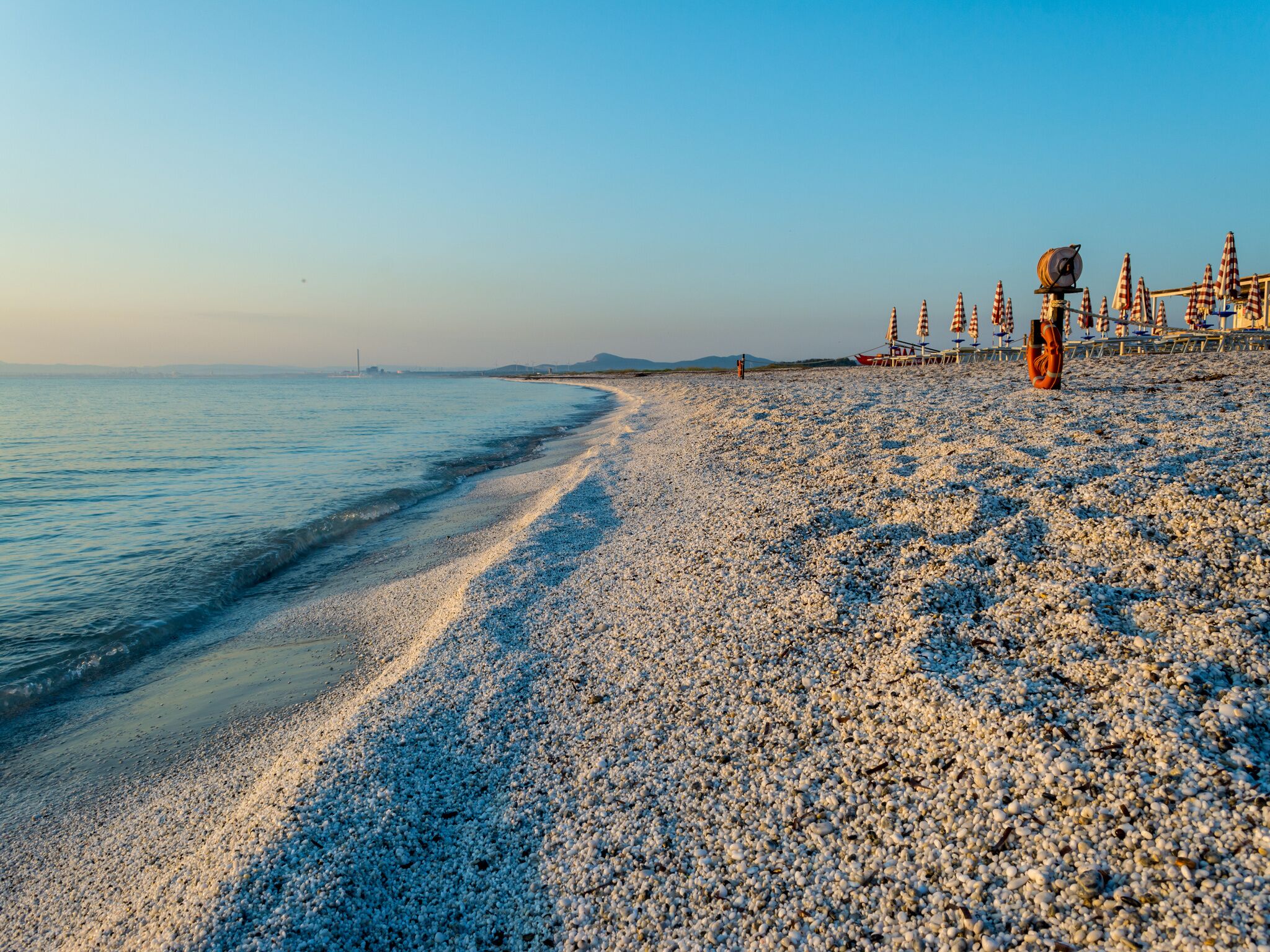 A pebble beach with a boat and umbrellas.