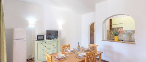 A dining area with a table set for four, a microwave, a refrigerator, and a television on a cabinet.