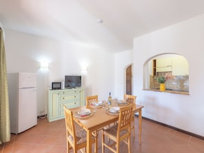 A dining area with a table set for four, a microwave, a refrigerator, and a television on a cabinet. - Comfortable and Bright Apartment (Stintino)
