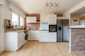 A modern kitchen with a built-in washing machine, a stove, and a refrigerator. - L'Alma du Laudon - Centre village et climatisation (Saint-Jorioz)