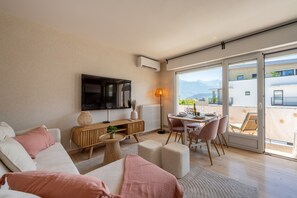 A modern living room with a sofa, a TV, a dining area, and a view of the mountains through large windows. - L'Alma du Laudon - Centre village et climatisation (Saint-Jorioz)