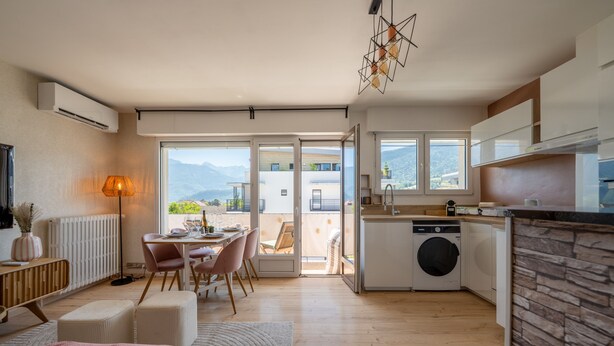 A modern kitchen with a built-in washing machine, a dining area with a table and chairs, and a view of the outdoors through large windows. - L'Alma du Laudon - Centre village et climatisation (Saint-Jorioz)