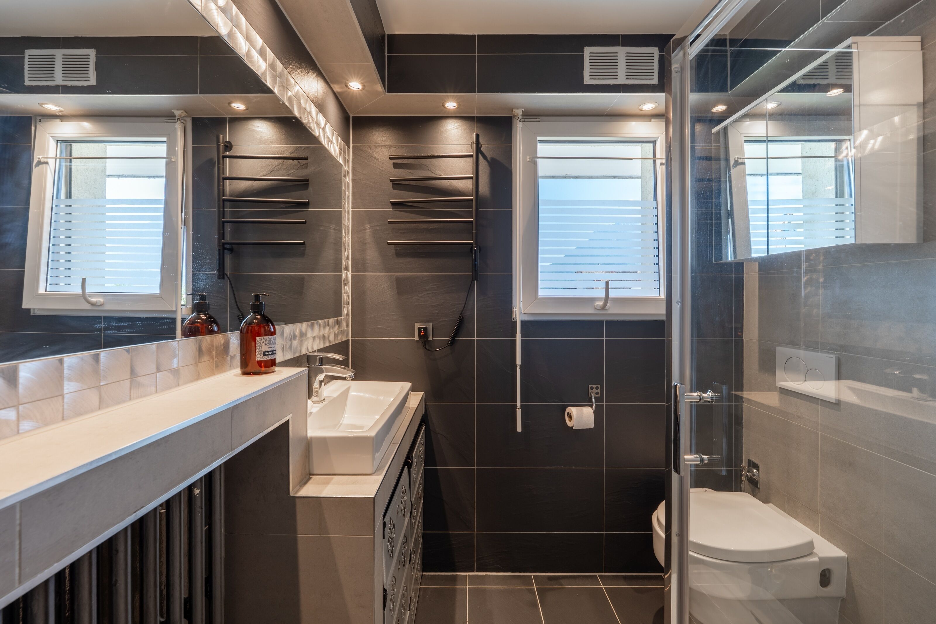 Et moderne badeværelse med en glas brusekabine, en hvid vask og et toilet.
