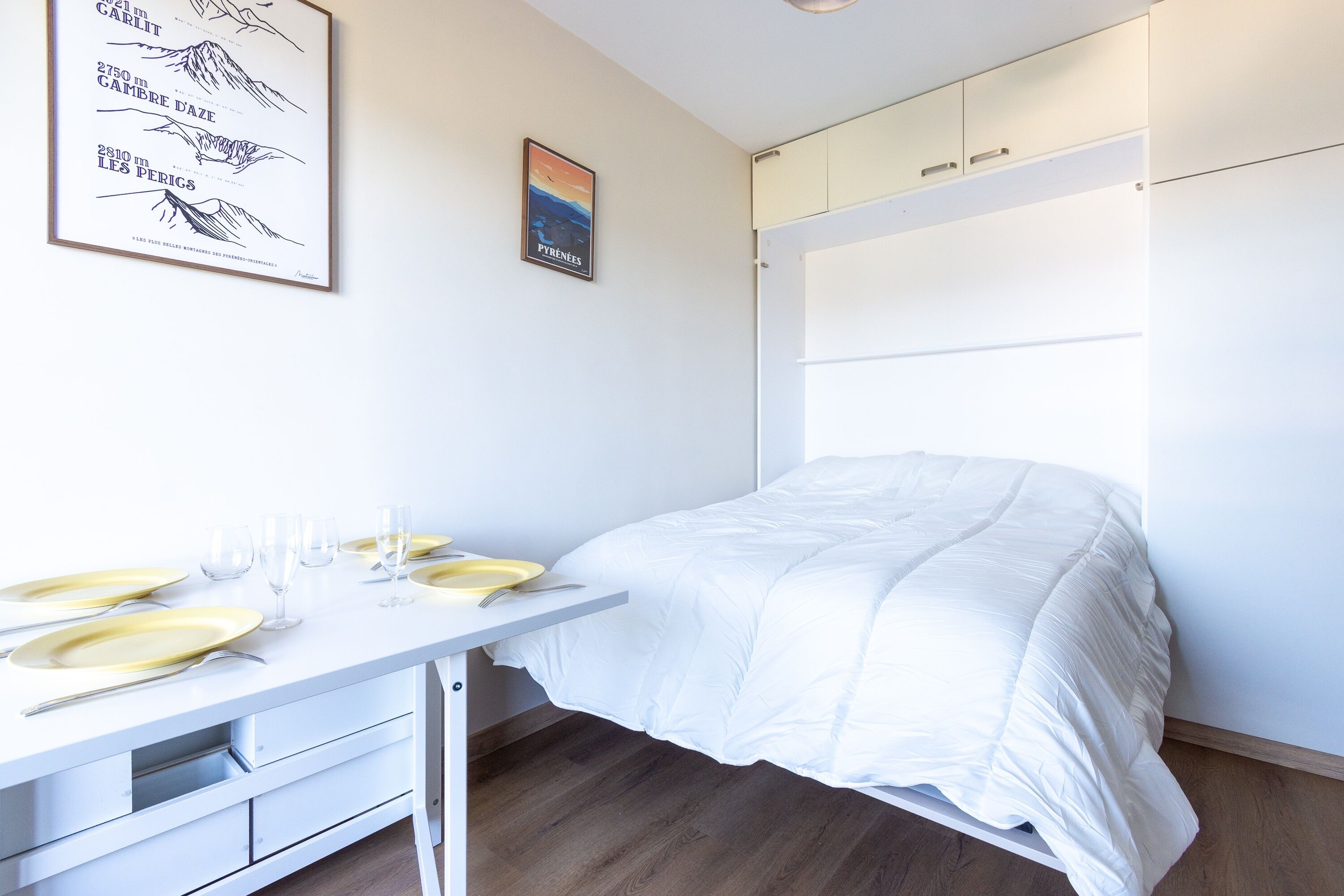 Une pièce bien rangée, avec un lit, une table mise pour le repas et une carte encadrée accrochée au mur.
