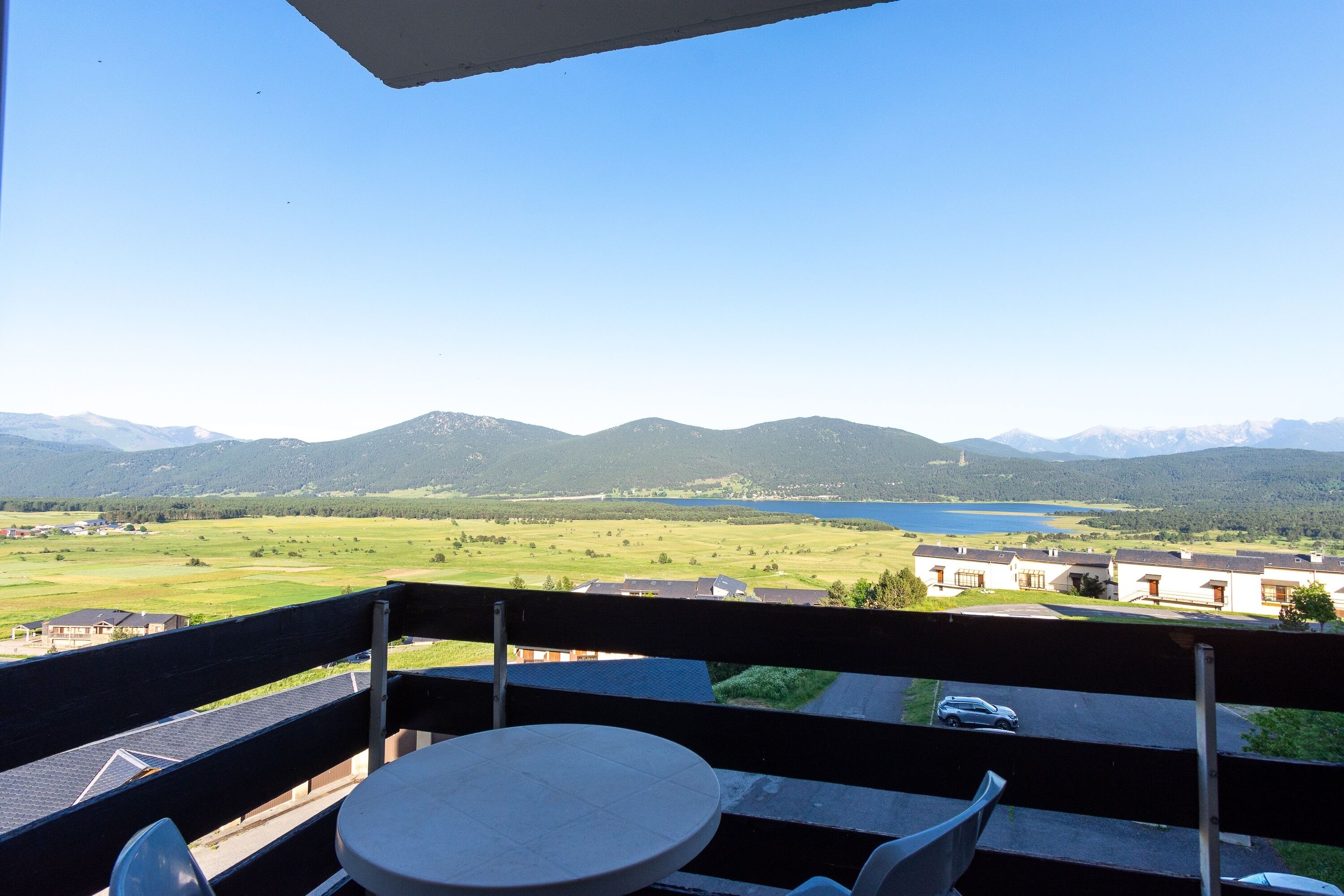 A balcony with a table and chairs, overlooking a scenic landscape with mountains and a lake.