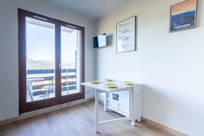 Ein Zimmer mit einem weißen Schreibtisch, einem an der Wand befestigten Fernseher und einem großen Fenster mit Bergblick.