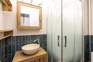 Un baño con tocador de madera, un espejo grande y mampara de vidrio para la ducha.