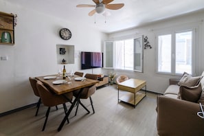 A modern living room with a dining area, a ceiling fan, a wall clock, and a large window. - La Maison Gecko Montfrin - Proche du Pont du Gard (Montfrin)