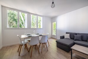 A modern living space with a dining area, a sofa, and large windows. - La Parenthèse Toulousaine - À 200 m du métro (Toulouse)