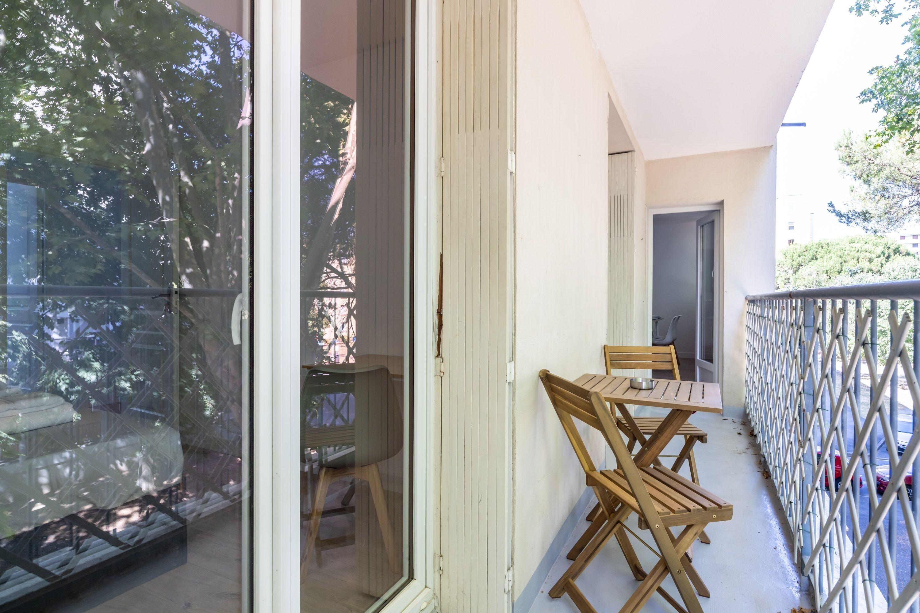 Un balcón con puerta de vidrio, sillas de madera y una mesa.