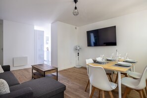 Un salon moderne avec un canapé, une table à manger pour quatre personnes, un téléviseur à écran plat et un ventilateur sur pied.