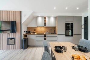 A modern kitchen with a dining area, featuring a wooden countertop, grey cabinets, and a built-in oven. - Suite Briance - Joli duplex pour 4 avec balcon (Saint-Chaffrey)