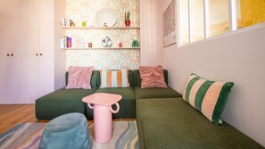 Ett mysigt vardagsrum med en grön soffa, ett rosa bord och en randig kudde.