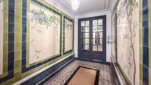 En hall med mönstrade kakelplattor, en dörr med glaspartier och en mönstrad matta på golvet.