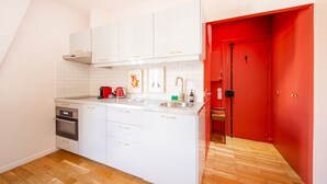 Cocina compacta con armarios blancos, un lavamanos de acero inoxidable, una puerta roja y un piso de madera con estampado tipo espiga.