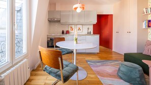 A modern kitchen with white cabinets, a round dining table, and a red accent wall. - Montmartre Flat - À 400 m du métro (Paris)