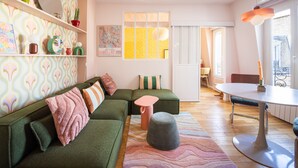 Una sala acogedora con un sofá verde, un taburete pequeño y una mesa de comedor con sillas.