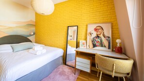 Hotelkamer met een bed, een bureau, een stoel, een spiegel en een wand met een geel baksteenpatroon.