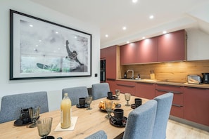 Ein moderner Essbereich mit Holztisch, grauen Stühlen und einem großen gerahmten Bild an der Wand.