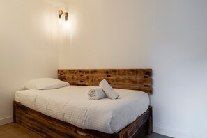 Ein Bett mit Holz-Kopfteil, weißer Bettwäsche und einem zusammengerollten Handtuch darauf.