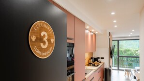 A modern kitchen with a large window, a black wall with a wooden plaque, and a view of greenery outside. - Suite Cucumelle - Beau Duplex pour 6 avec balcon (Saint-Chaffrey)